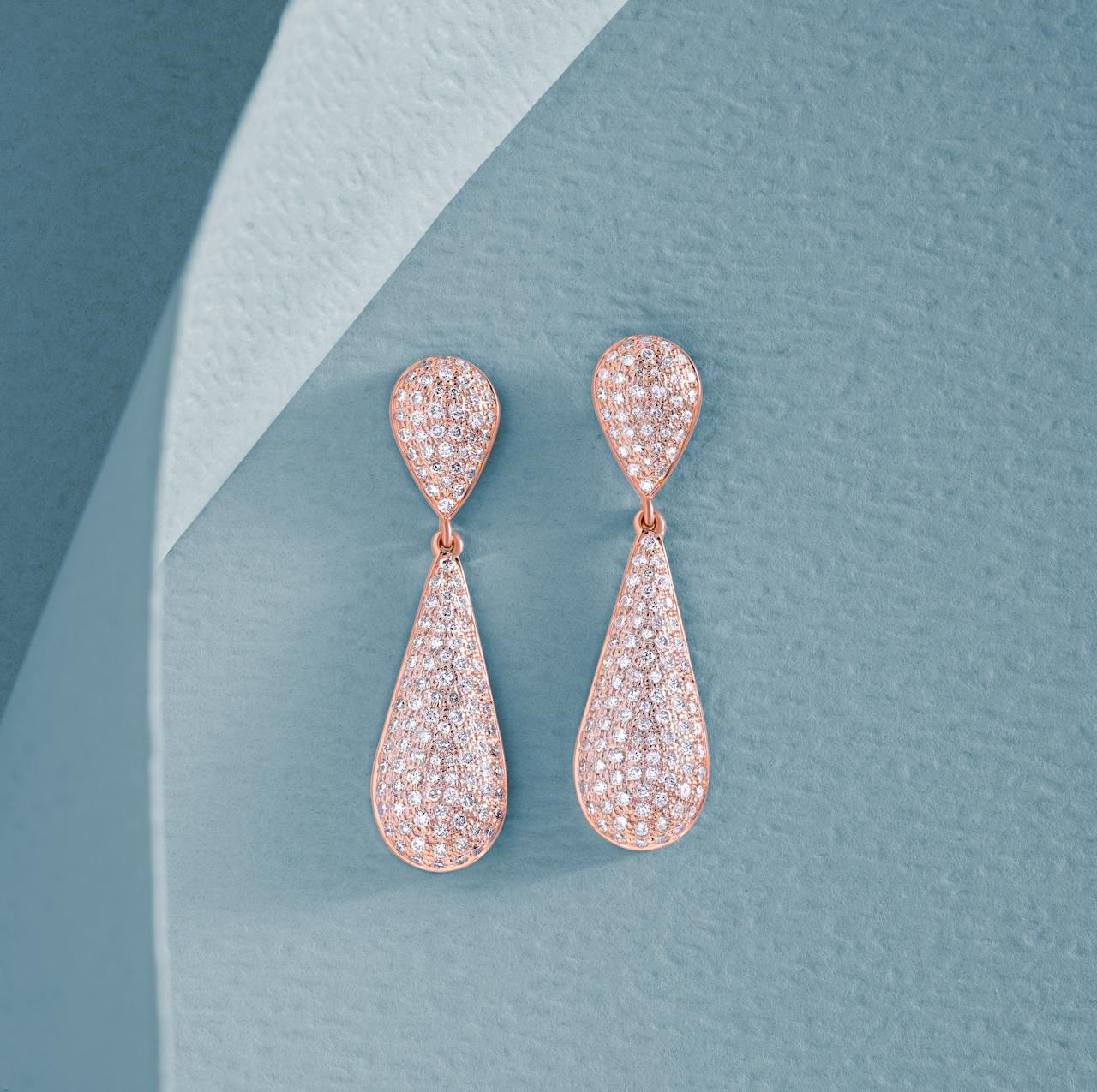 Close-up of diamond-encrusted dangling earrings on a textured blue background, highlighting luxury and elegance.